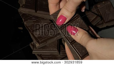 Woman Holds Black Chocolate Bar. Close-up Shot Of Woman Fingers With The Chocolate