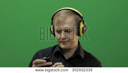 Guy Listens To Music In Wireless Yellow Headphones. Portrait Of Attractive Man Using Smart Phone For