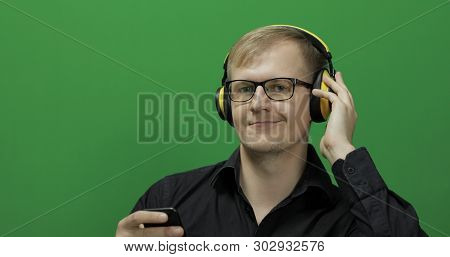 Guy Listens To Music In Wireless Yellow Headphones. Portrait Of Attractive Man Using Smart Phone For