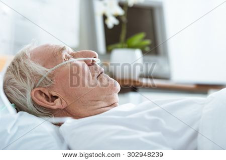 Side View Of Senior Man In Coma On Bed In Hospital