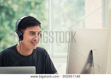 Student Learning Online Study Concept: Asian Young Man Listening With Headphones And Laptop, Sitting