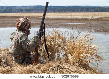 Duck Hunter With A Shotgun Sitting Next To The Blind Of Reeds On The Lake