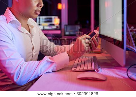 Young Office Worker In White Shirt Sitting At Office Desk And Typing A Message On Mobile Phone While