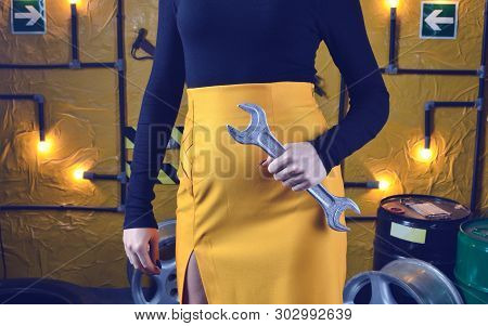 Fashionable Mechanic Girl In Trendy Clothes Is Holding A Wrench On The Background Of The Workshop Of