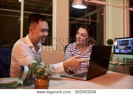 Smiling Asian Businessman Pointing At Monitor Of Laptop Computer And Talking With Businesswoman List