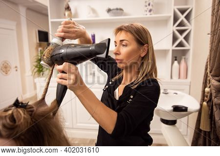 Pretty Adult Woman Hairdresser Enjoying Working In Beauty Salon And Blowdrying Hair Of Customer