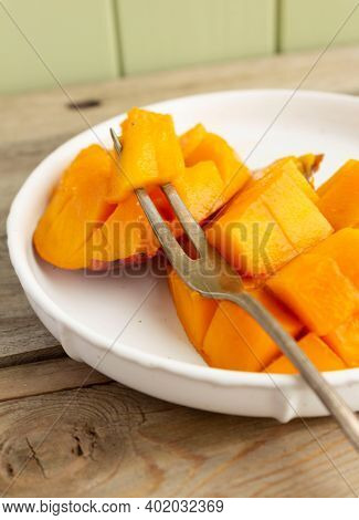 Sliced Juicy Mango Fruit Of Orange Color On The White Plate With Horn Fruit Fork On The Rustic Woode