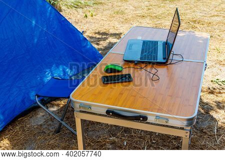 Laptop With Computer Mouse And Smartphone On A Folding Picnic Table In A Camping. Working While Trav