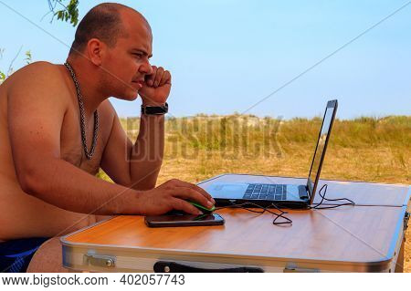 Man Using His Laptop Sitting At A Folding Picnic Table In A Camping. Working While Traveling. Freela