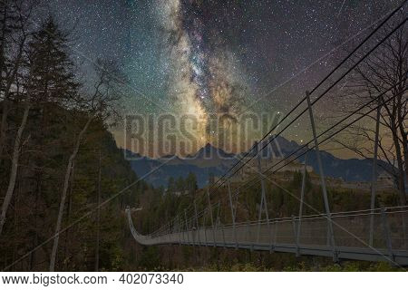 Suspension Bridge With Trees In Front Of Mountains And A Castle With Milky Way