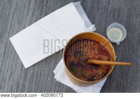 Asian Food In Craft Packaging With A Spoon And Napkins On A Wooden Bench.