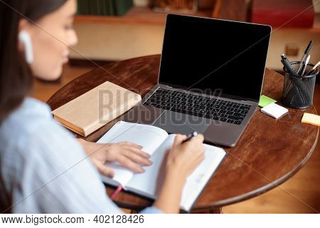 Distant Work Or Education Concept. Over The Shoulder View Of Young Woman Wearing Earbuds Sitting At 