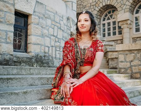 Young Beautiful Indian Woman Walks On Ancient Architecture Streets Of City Of India Dressed In Red S
