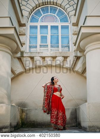 Young Beautiful Indian Woman Dancing In Red Sari On Background Walls Ancient Building Outdoors.