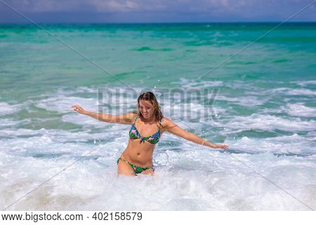 Young Beautiful Girl Enjoys The Sea And The Waves, Laughing Raising Her Hands Up In A Black Fashiona