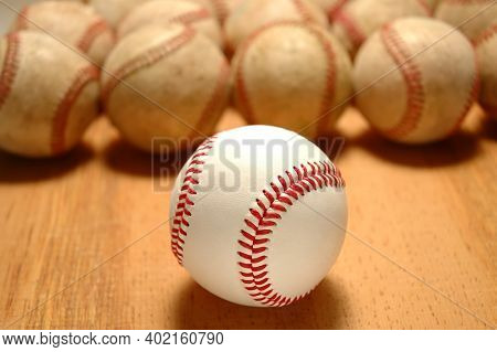 Closeup of a new baseball on in front of a row of old use balls, focus on the front ball.