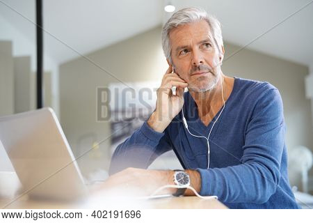 Senior man working on laptop and using earphones for virtual meeting