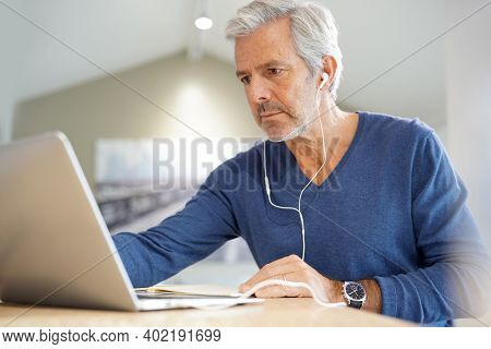 Senior man working on laptop and using earphones for virtual meeting