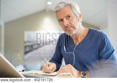 Senior man working on laptop and using earphones for virtual meeting