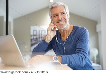 Senior man working on laptop and using earphones for virtual meeting
