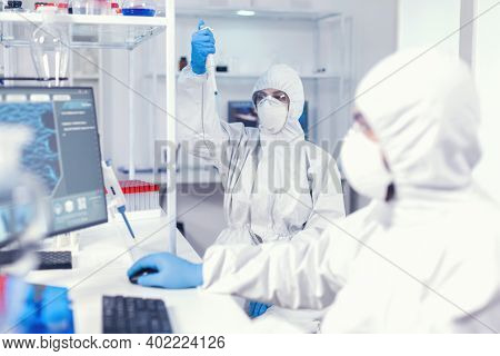 Woman Scientist In Coverall Using Micropipette In Lab For Coronavirus Research. Team Of Microbiologi