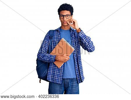 Young african american man wearing student backpack holding book mouth and lips shut as zip with fingers. secret and silent, taboo talking 