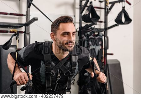 Young Smiling Athlete In Ems Suit Training With Suspension Rope