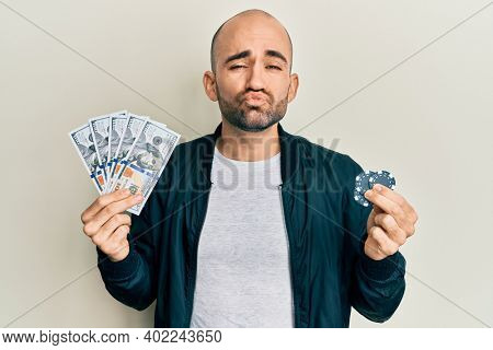 Young hispanic man playing poker holding dollars banknotes and chips looking at the camera blowing a kiss being lovely and sexy. love expression. 