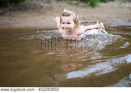 A Little Girl Is Swimming In The River In Shallow Water. Shes Lying On Her Stomach With Her Arms Pul