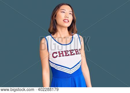 Young beautiful chinese girl wearing cheerleader uniform looking away to side with smile on face, natural expression. laughing confident. 