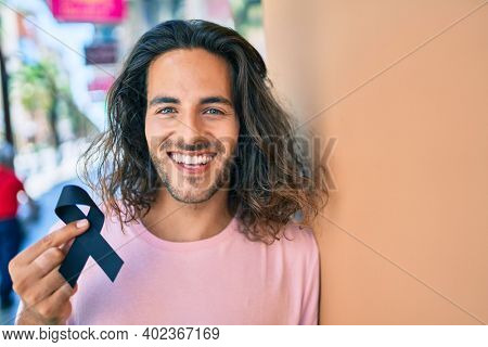 Young hispanic man smiling happy holding mouring black ribbon leaning on the wall.