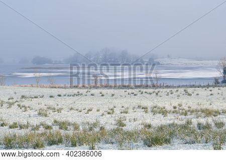 Winter View On The Lake With Frozen Grass At Foreground.
