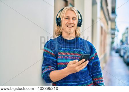 Young scandinavian student man smiling happy using smartphone and headphones at the city.