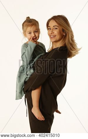 Little Daughter And Mom In Black Pant Suit And Blue Dress Hug Close Up Studio Portrait Isolated On W