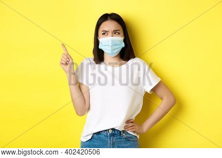Covid, Health Care And Pandemic Concept. Asian Woman In Medical Mask And White T-shirt Pointing Fing