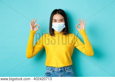 Covid-19, Social Distancing And Pandemic Concept. Smiling Confident Asian Woman In Medical Mask Show