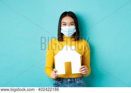 Covid-19, Pandemic And Real Estate Concept. Cheerful Asian Woman Smiling In Medical Mask, Showing Pa