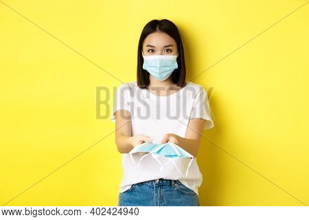 Coronavirus, Quarantine And Medicine Concept. Cute Asian Girl Giving Medical Masks And Looking At Ca