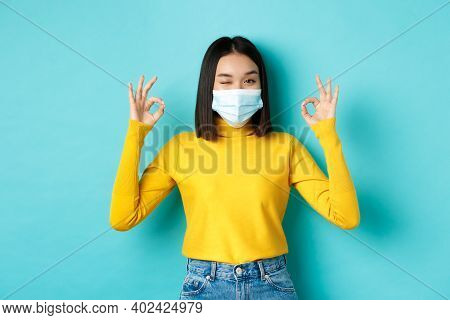 Covid-19, Social Distancing And Pandemic Concept. Cheerful Asian Girl In Medical Mask Showing Okay G
