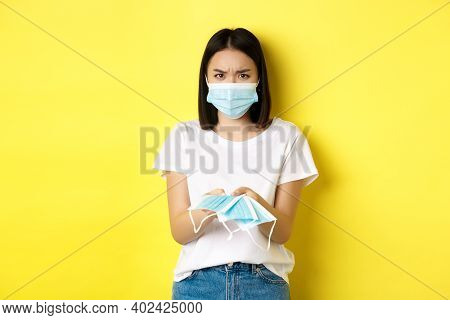 Coronavirus, Quarantine And Medicine Concept. Angry Asian Girl Giving You Medical Mask Indoors, Frow
