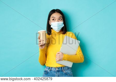 Covid-19, Health Care And Quarantine Concept. Asian Girl Student In Medical Mask Standing With Lapto