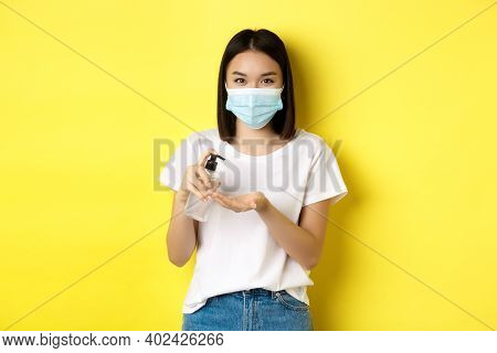 Covid, Health Care And Pandemic Concept. Cute Asian Woman In Medical Mask Using Hand Sanitizer To Di