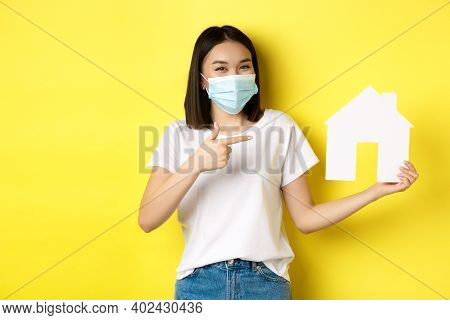 Covid-19, Pandemic And Real Estate Concept. Cheerful Asian Woman Smiling In Medical Mask, Showing Pa