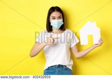 Covid-19, Pandemic And Real Estate Concept. Cheerful Asian Woman Smiling In Medical Mask, Showing Pa