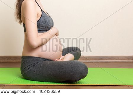Beautiful Young Pregnant Woman Sitting On Mat In Yoga Pose At The Home. Pregnancy Yoga And Fitness C