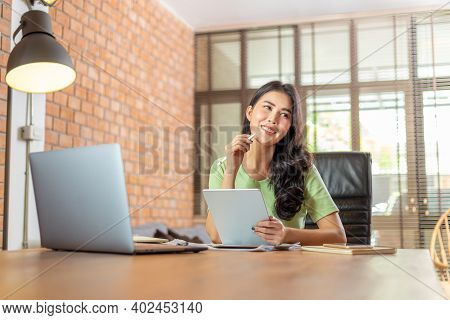Happy Young Asian Businesswoman Siting In Her Home Living Room Office Smiling While Thinking Of Her 