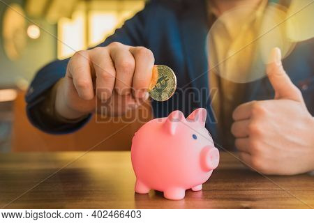 The Hand Of A Businessman Holds A Golden Bitcoin Cryptocurrency Next To A Pig Piggy Bank. Bitcoin, C