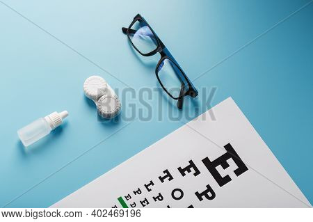 Glasses With Contact Lenses, Drops And An Optometrist's Eye Test Chart On A Blue Background.