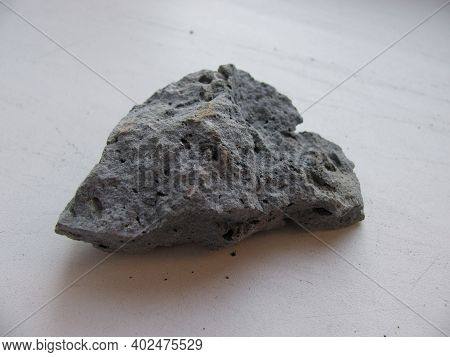 A Piece Of Gray Basalite On A Beige Table. A Mineral Resource.