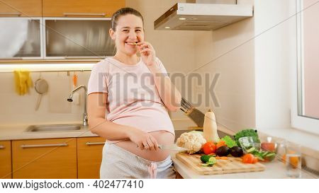 Portrait Of Happy Smiling Pregnant Woman Cooking On Kitchen And Wating Fresh Tasty Vegetables. Conce